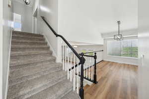 Stairs with wood finished floors, high vaulted ceiling, a notable chandelier, and baseboards