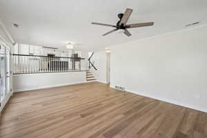 Empty room with light wood-type flooring, ceiling fan, visible vents, and stairs