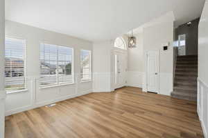 Foyer with light wood-style floors, wainscoting, visible vents, and stairs