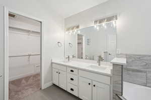 Full bath with toilet, double vanity, a sink, and baseboards