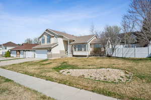 View of front of property featuring a front yard, an attached garage, concrete driveway, fence, and stucco siding