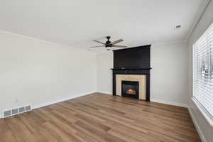 Unfurnished living room with ornamental molding, visible vents, ceiling fan, and wood finished floors