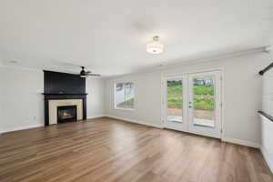 Unfurnished living room with a large fireplace, baseboards, a ceiling fan, and wood finished floors