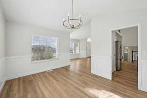Unfurnished dining area with an inviting chandelier, visible vents, wainscoting, lofted ceiling, and light wood finished floors