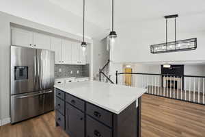 Kitchen featuring stainless steel fridge with ice dispenser, a ceiling fan, white cabinetry, wood finished floors, and backsplash