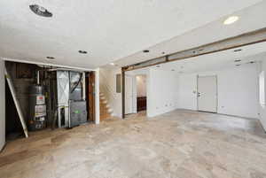 Finished below grade area with a textured ceiling, heating unit, stairway, and water heater