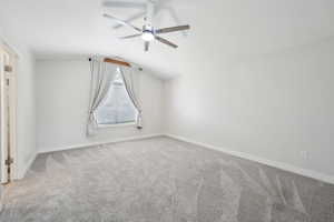 Carpeted empty room featuring baseboards, a ceiling fan, and vaulted ceiling