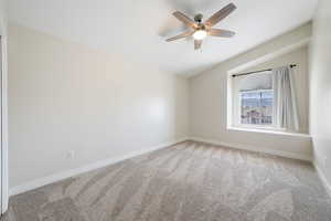 Spare room featuring light carpet, lofted ceiling, baseboards, and ceiling fan