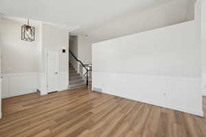Interior space featuring stairway, light wood-style flooring, a wainscoted wall, visible vents, and lofted ceiling