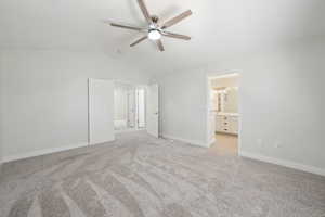 Unfurnished bedroom with connected bathroom, light colored carpet, a ceiling fan, vaulted ceiling, and baseboards