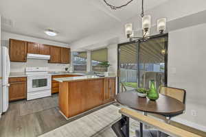 Kitchen with light countertops, white appliances, a peninsula, under cabinet range hood, and wood finished floors