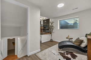 Sitting room with visible vents, a chandelier, wood finished floors, an upstairs landing, and baseboards