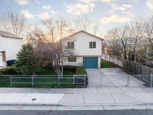 View of front facade featuring concrete driveway, a front yard, a garage, and a fenced front yard