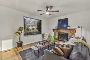 Living area featuring baseboards, a fireplace, visible vents, ceiling fan, and wood finished floors
