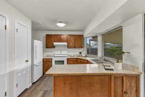 Kitchen featuring white appliances, a peninsula, light countertops, under cabinet range hood, and a sink