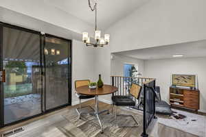 Dining area featuring vaulted ceiling, visible vents, a chandelier, wood finished floors, and baseboards