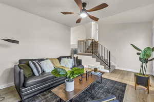 Living room with wood finished floors, ceiling fan, baseboards, and stairs