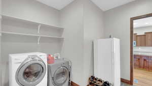 Washroom with light wood-style flooring, washer and clothes dryer, laundry area, and baseboards