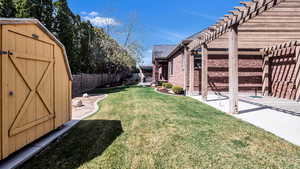 View of yard with a pergola, a patio area, a fenced backyard, an outdoor structure, and a storage unit