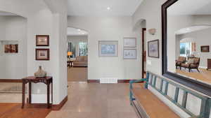 Hall with arched walkways, visible vents, plenty of natural light, baseboards, and stone tile flooring