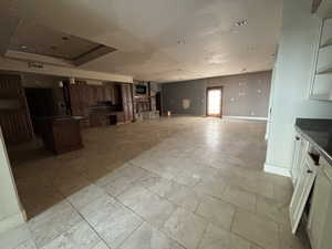 Unfurnished living room with a raised ceiling and light stone finish flooring