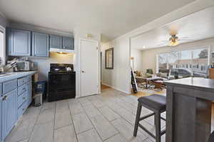 Kitchen with tile counters, blue cabinetry, electric range, a ceiling fan, and under cabinet range hood