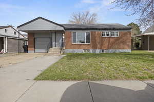 View of front of home with brick siding, a front yard, an attached garage, and concrete driveway