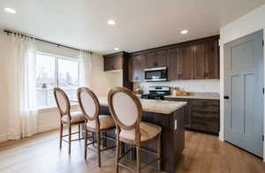 Kitchen with a breakfast bar, recessed lighting, dark brown cabinets, light wood-style floors, and appliances with stainless steel finishes