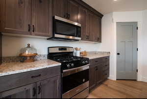 Kitchen featuring dark brown cabinets, light stone countertops, light wood-style floors, and stainless steel appliances