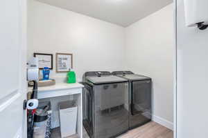 Washroom featuring baseboards, light wood-type flooring, washer and clothes dryer, and laundry area