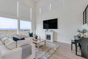 Living area featuring light wood-style flooring, a high ceiling, a glass covered fireplace, and baseboards