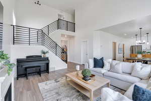 Living area featuring light wood-style floors, an inviting chandelier, a towering ceiling, visible vents, and stairway