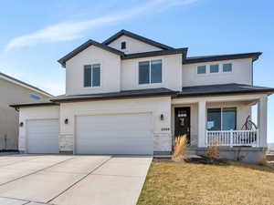 View of front facade featuring a porch, stone siding, a garage, concrete driveway, and stucco siding