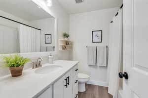 Full bathroom featuring vanity, baseboards, toilet, visible vents, and wood finished floors