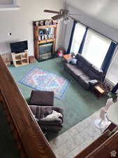 Living area with a glass covered fireplace, tile patterned floors, carpet, and a ceiling fan