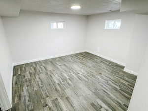 Basement with a textured ceiling, a healthy amount of sunlight, wood finished floors, and baseboards