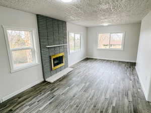 Unfurnished living room featuring baseboards, a textured ceiling, wood finished floors, and a fireplace