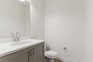 Half bath with vanity, baseboards, toilet, and wood finished floors