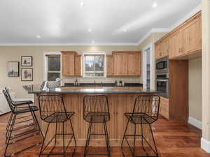 Kitchen with a kitchen breakfast bar, recessed lighting, crown molding, stainless steel appliances, and wood finished floors