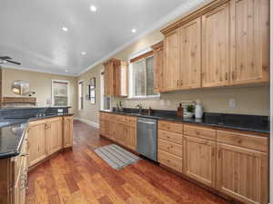 Kitchen featuring light brown cabinets, ornamental molding, stainless steel dishwasher, light wood finished floors, and a sink