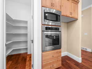 Kitchen featuring dark wood-style flooring, light brown cabinets, baseboards, and stainless steel appliances and walk-in pantry.
