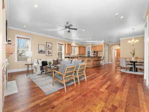 Living area featuring light wood-style flooring, ceiling fan with notable chandelier, and crown molding