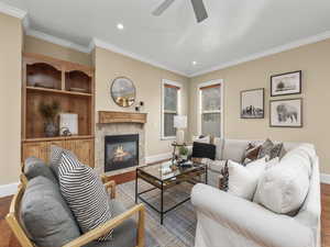 Living room featuring ornamental molding, a ceiling fan, wood finished floors, a tile fireplace, and baseboards