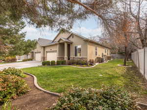 View of front of property with a garage, stucco siding, stone siding, fence, and driveway and mature trees