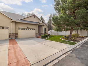 View of front of property featuring stone siding, a garage, concrete driveway, fence, and stucco siding and mature trees