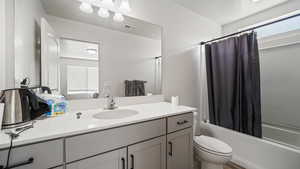 Bathroom featuring visible vents, toilet, shower / bathtub combination with curtain, and vanity