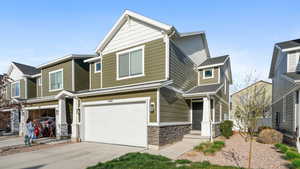 Craftsman house with an attached garage, stone siding, and driveway