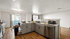 Kitchen with dark wood finished floors, gray cabinets, a chandelier, a sink, and stainless steel appliances