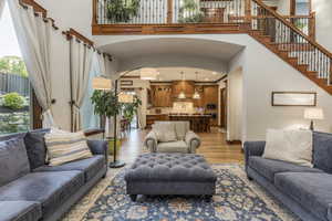 Living room with arched walkways, light wood finished floors, recessed lighting, a high ceiling, and stairs