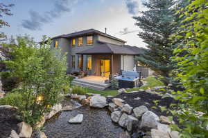 Back of house featuring a hot tub, a wooden deck, stucco siding, and a small pond